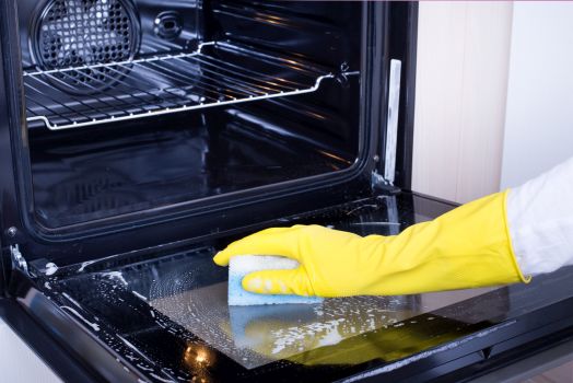 Kobieta w żółtej rękawiczce czyści gąbką piekarnik
