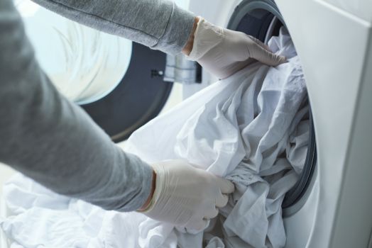 Kobieta w rękawiczkach wkłada pranie do pralki